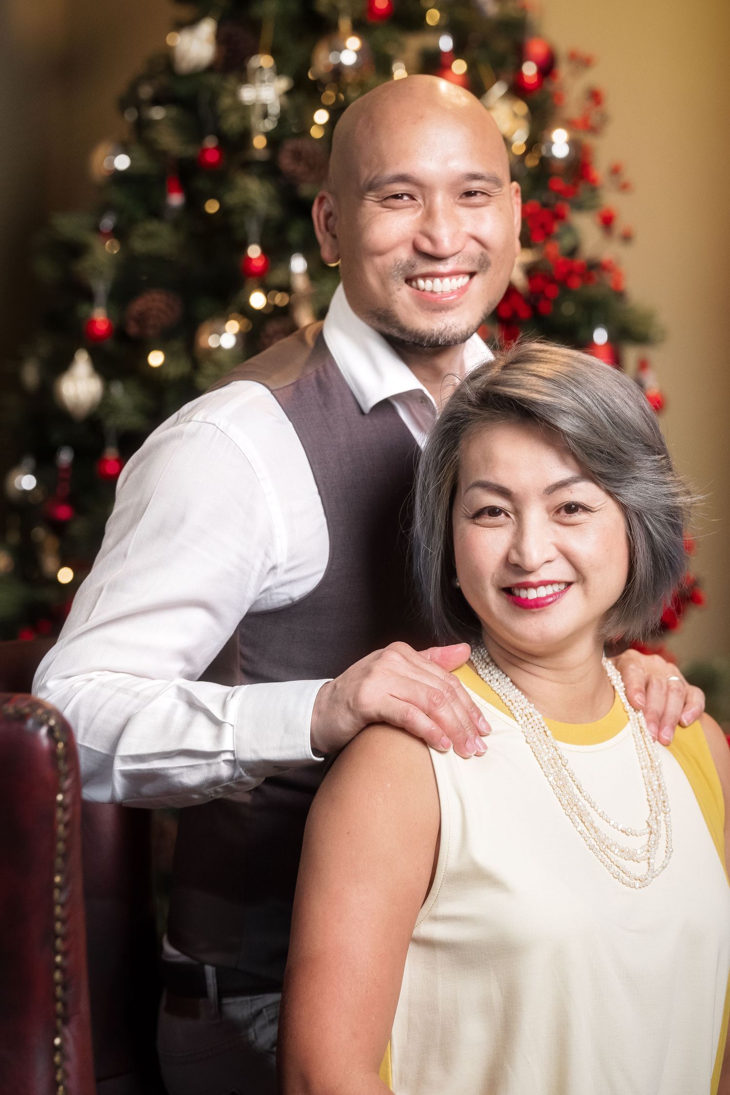 Smiling couple poses together in front of a decorated Christmas tree during the holiday season.