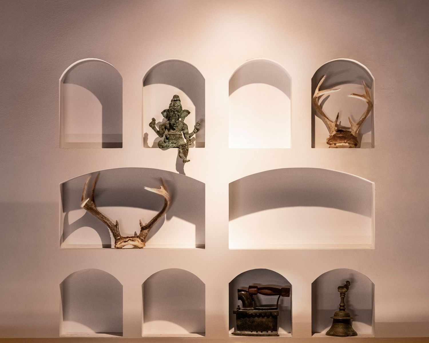 White wall display shelves with arched niches showcasing antlers, a bronze figurine, crab, and vintage typewriter.