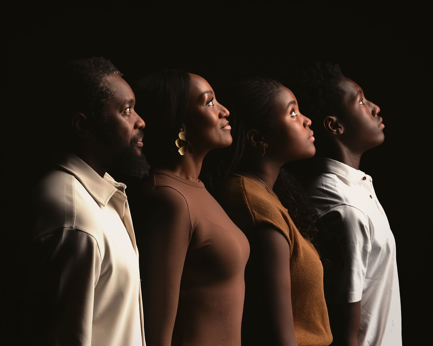 Four Black individuals stand in profile against a dark background, looking upward in a powerful portrait.
