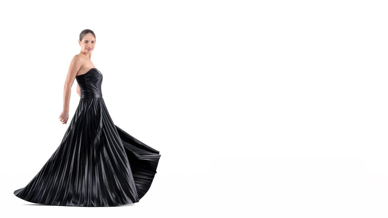 Woman posing in an elegant black strapless satin ball gown with a flowing pleated skirt on white background.