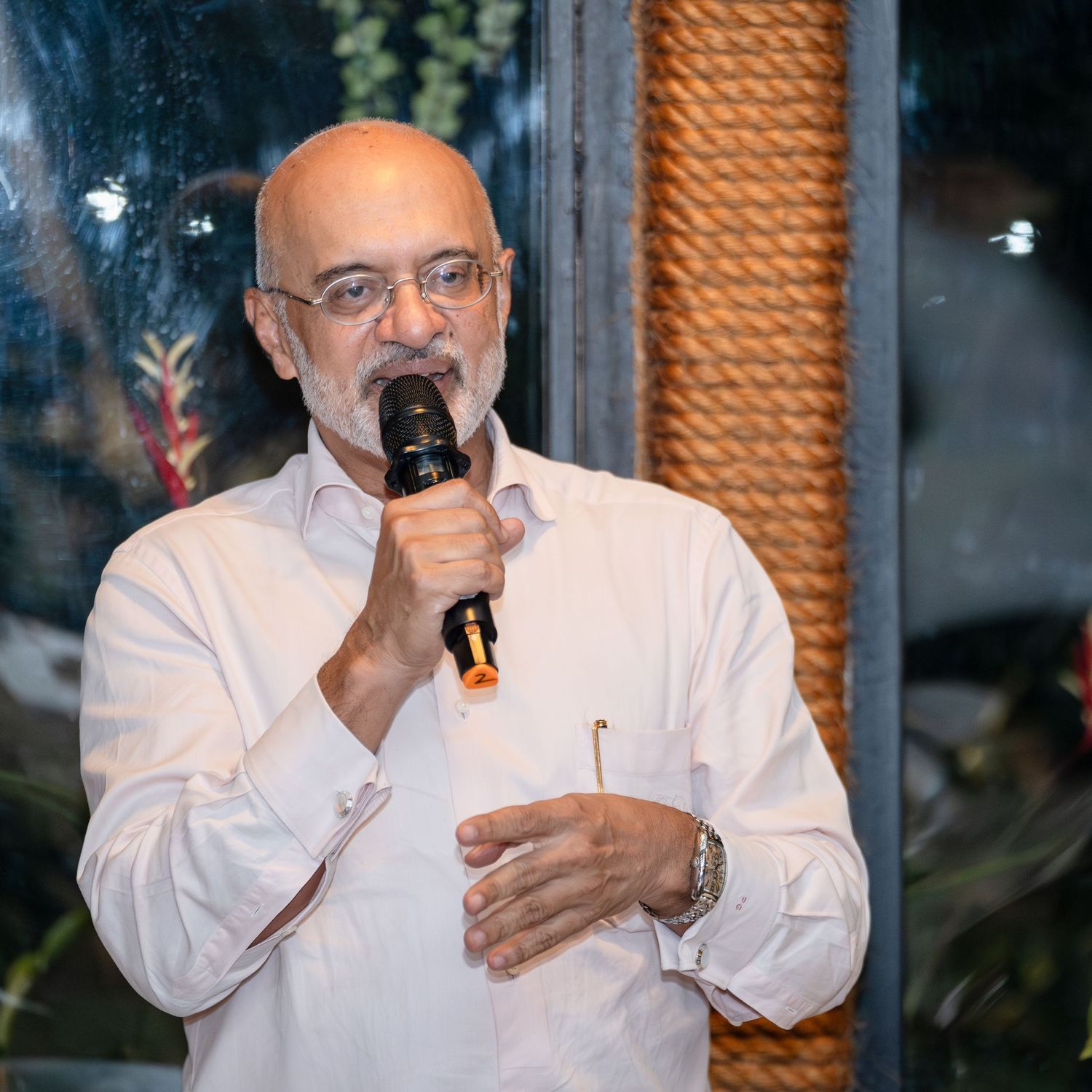 A bald man in a white shirt speaks into a microphone at an indoor event.