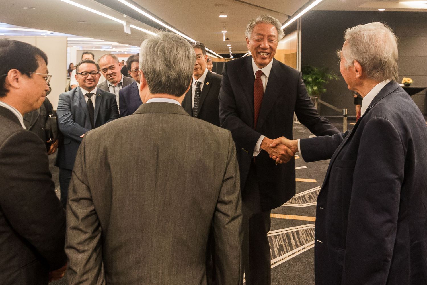 Business leaders exchange handshakes at a formal corporate or diplomatic networking event.