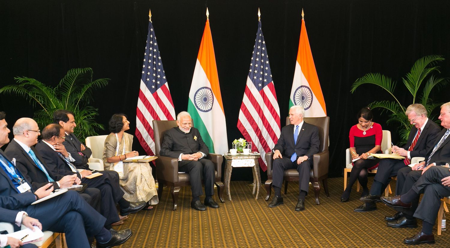 Indian PM Modi meets US President Biden in bilateral talks, flanked by officials with Indian and American flags.