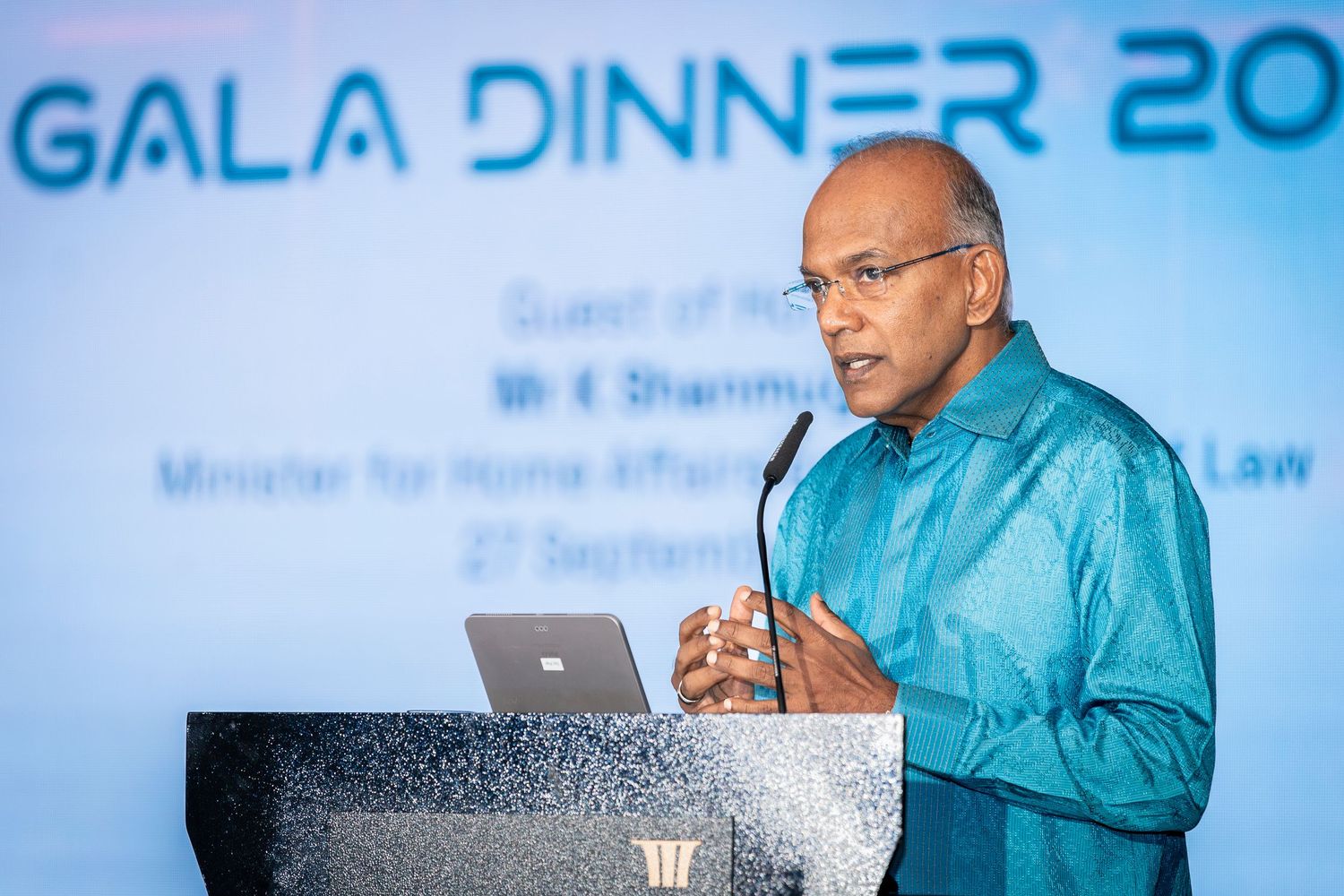 Minister K Shanmugam delivers speech at Gala Dinner 2023 podium in teal traditional attire.