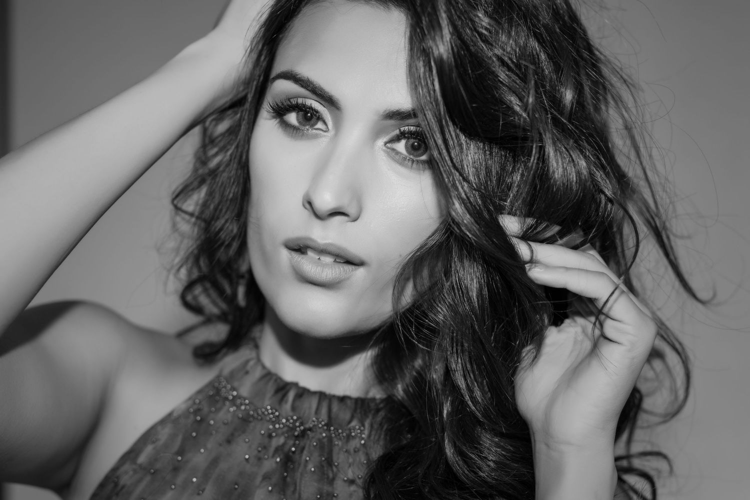 Black and white portrait of a young woman with curly hair posing elegantly with hands in hair.