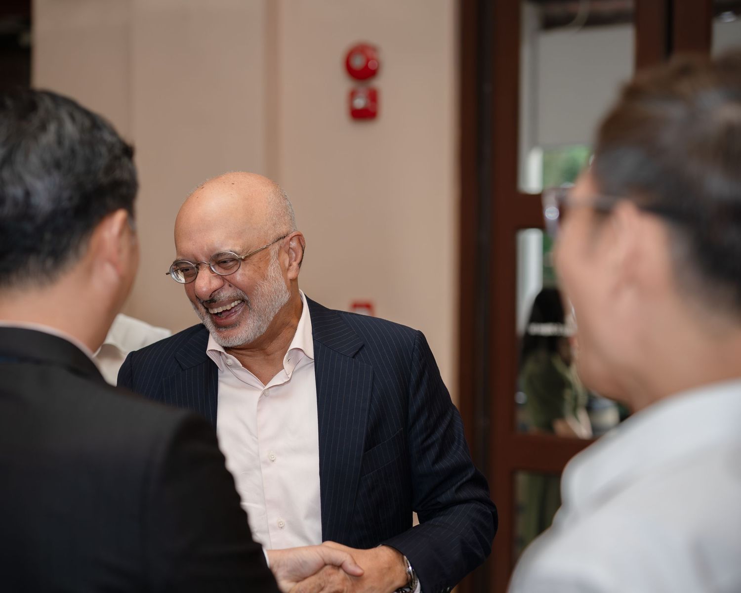 Business professional in navy blazer smiling and shaking hands at a networking event indoors.