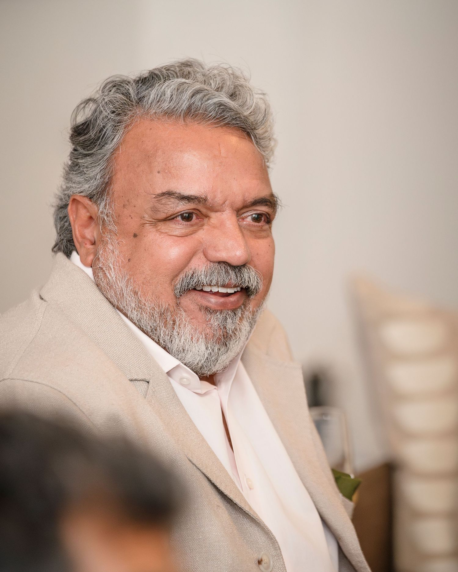 Smiling middle-aged man with gray hair and beard wearing a beige blazer at an indoor event.
