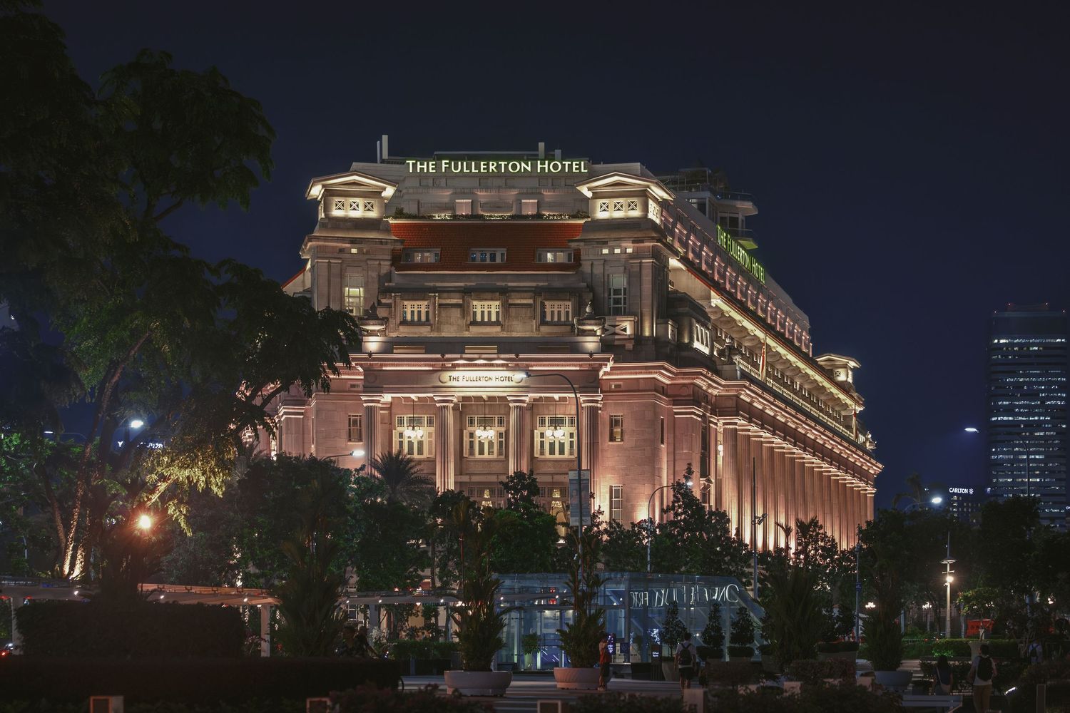 The Fullerton Hotel Singapore illuminated at night, showcasing its grand neoclassical architecture against a dark sky.