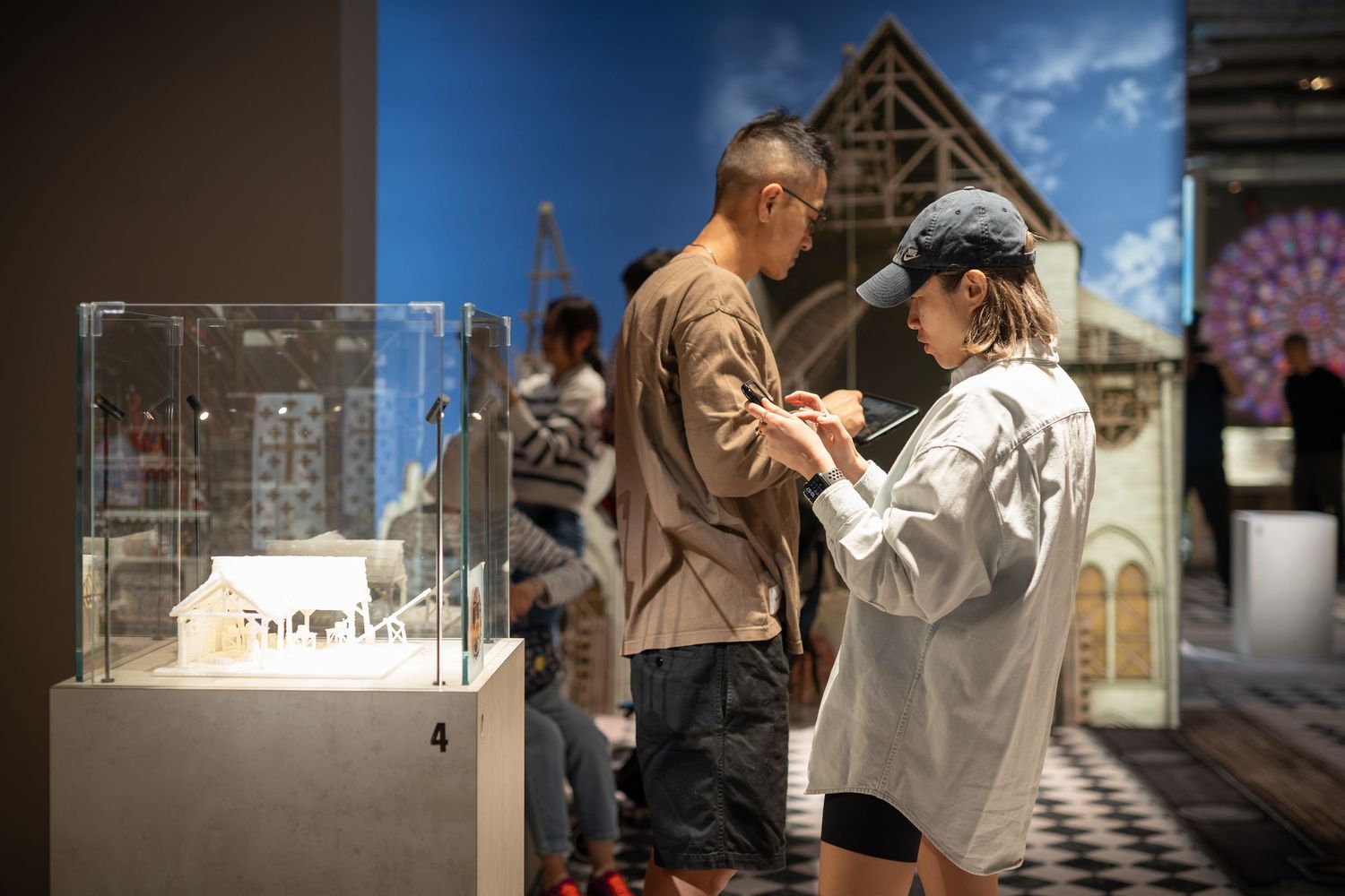 Museum visitors examining a detailed architectural scale model inside a modern exhibition gallery.