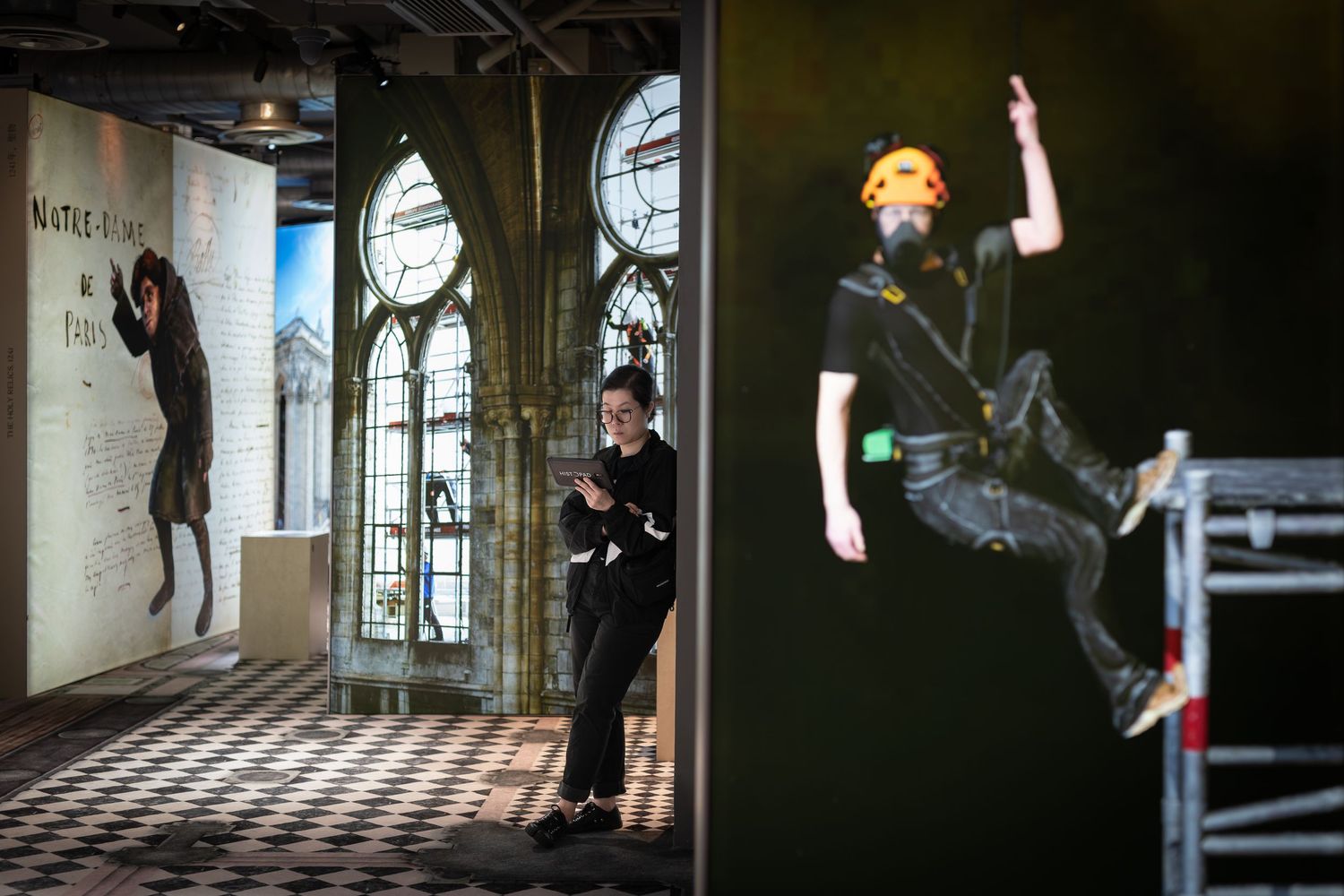 Exhibition worker standing near large wall murals depicting gothic cathedral windows and a suspended figure display.