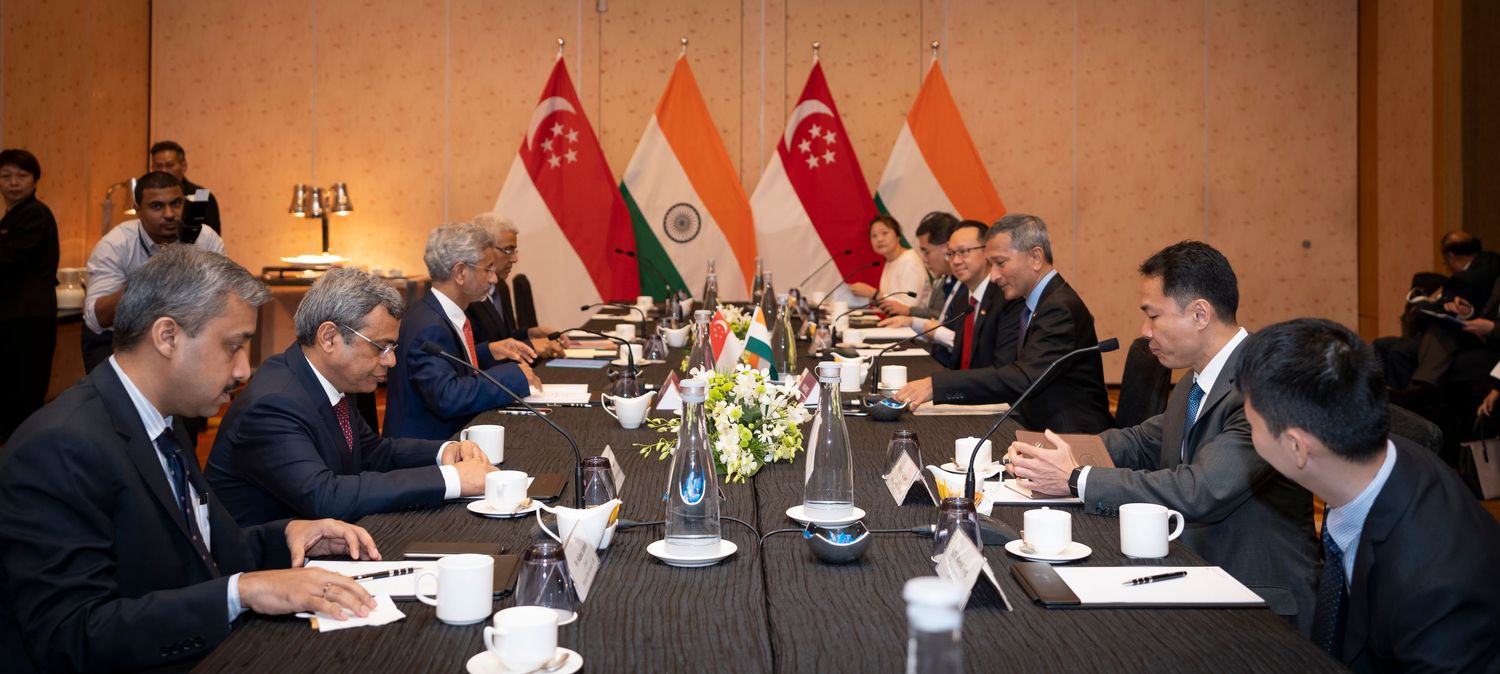 Diplomats from India and Singapore engage in a formal bilateral meeting at a conference table with national flags.