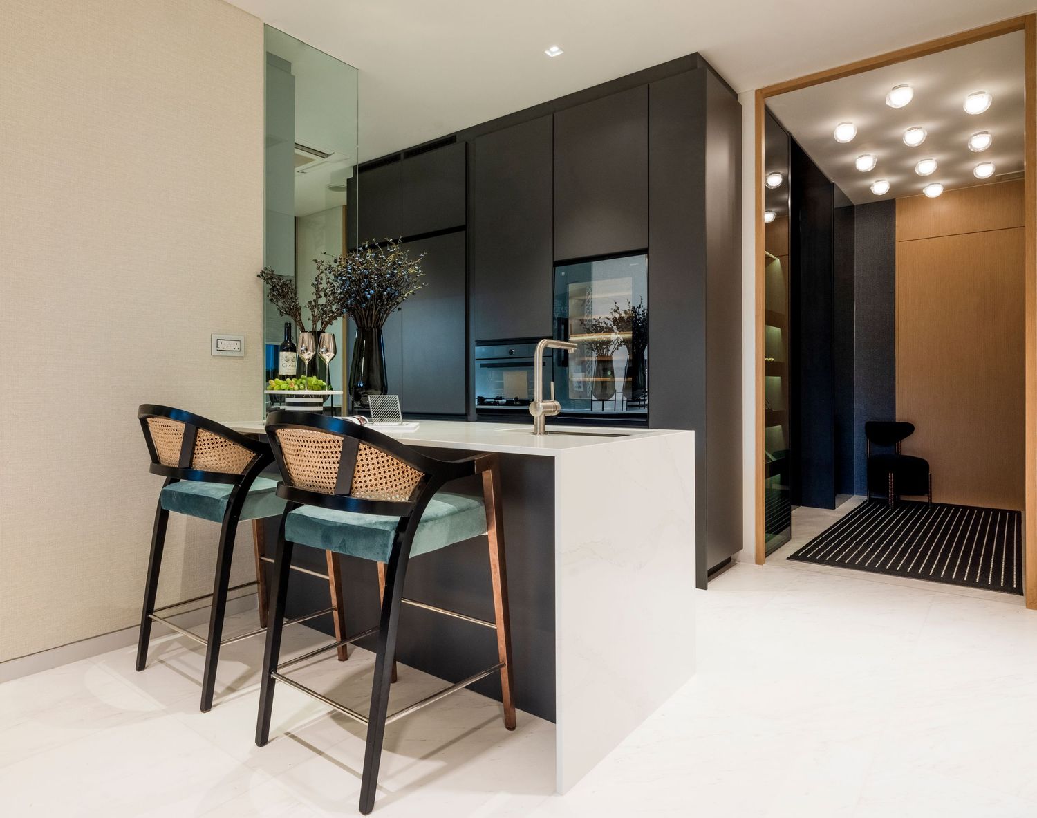 Modern kitchen with black cabinetry, white countertop island, and two stylish bar stools with teal cushions.