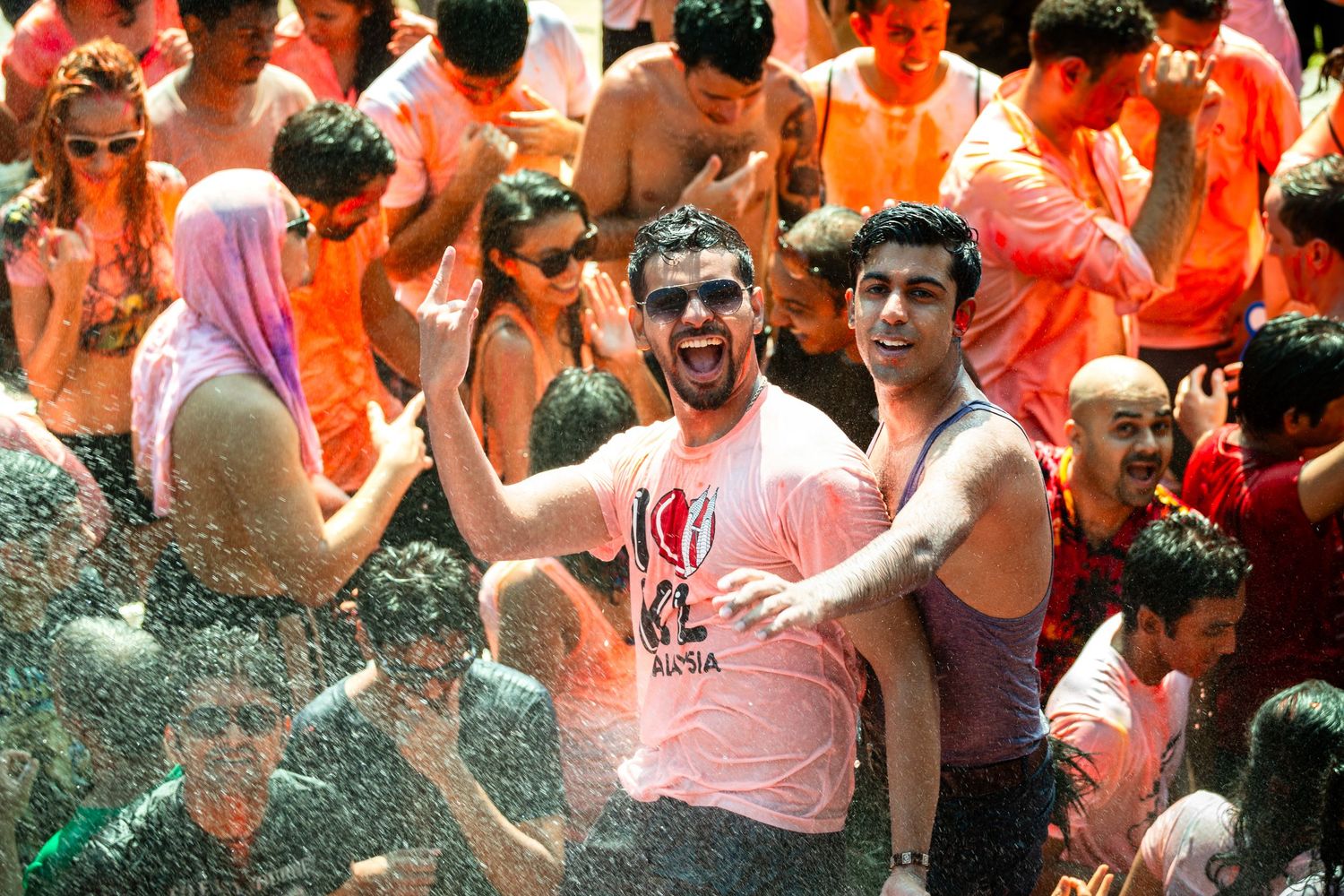 Crowd of people celebrating outdoors, drenched in colorful water during festive street event.
