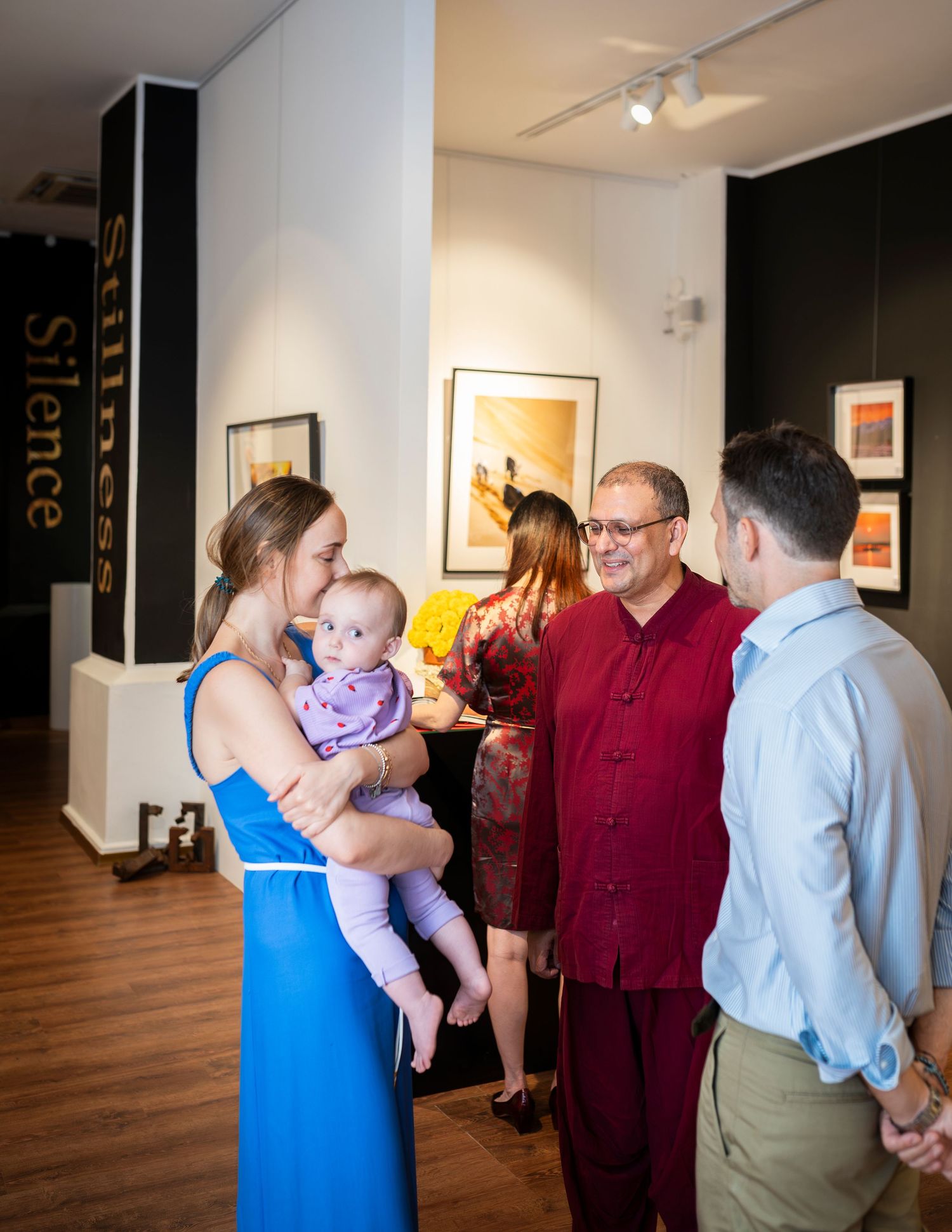 People socializing at an art gallery opening with a woman holding a baby talking to guests.