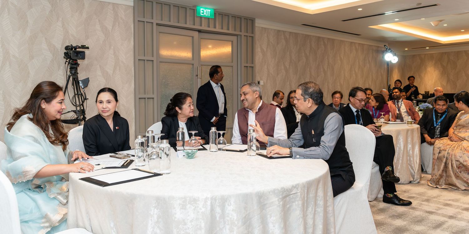 Professionals in formal attire seated at round tables during a conference or diplomatic meeting in an elegant banquet hall.
