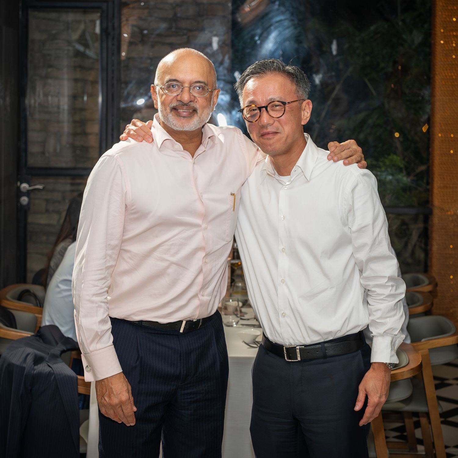 Two men in white shirts smiling and posing together at an indoor restaurant event.