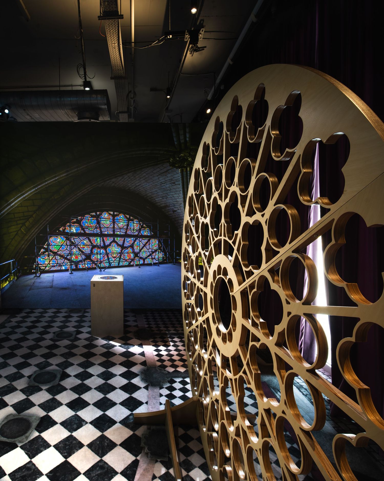 Gothic-inspired interior with ornate circular wooden screen, stained glass arch window, and black-and-white checkered floor.