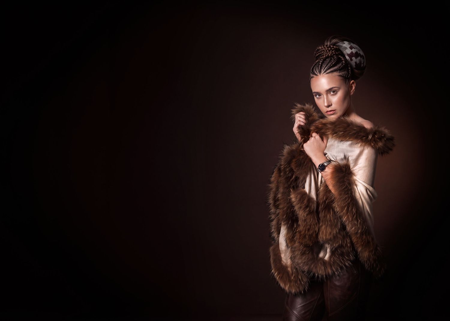 Woman in fur wrap with braided updo poses elegantly against dark background in fashion portrait.