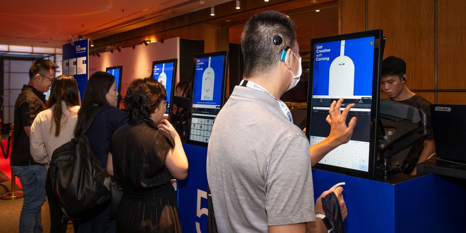 People interact with digital kiosks displaying bottle graphics at a tech expo event in a modern venue.