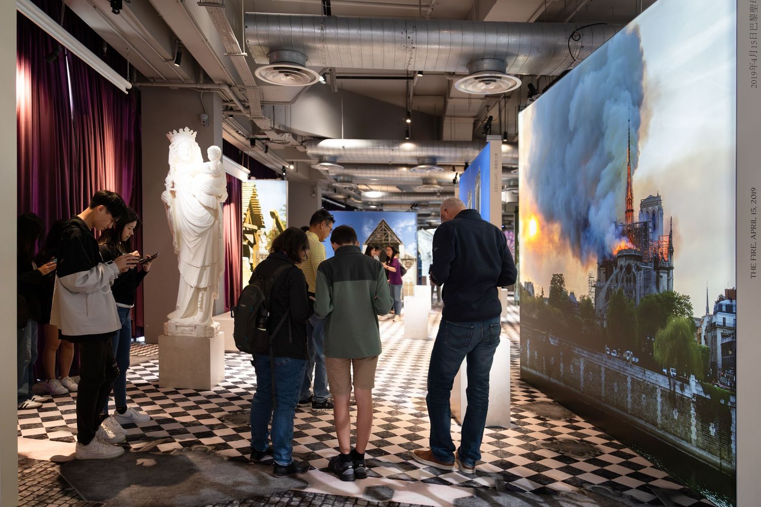 Visitors walk through an immersive exhibition featuring a large display of Notre Dame Cathedral on fire.