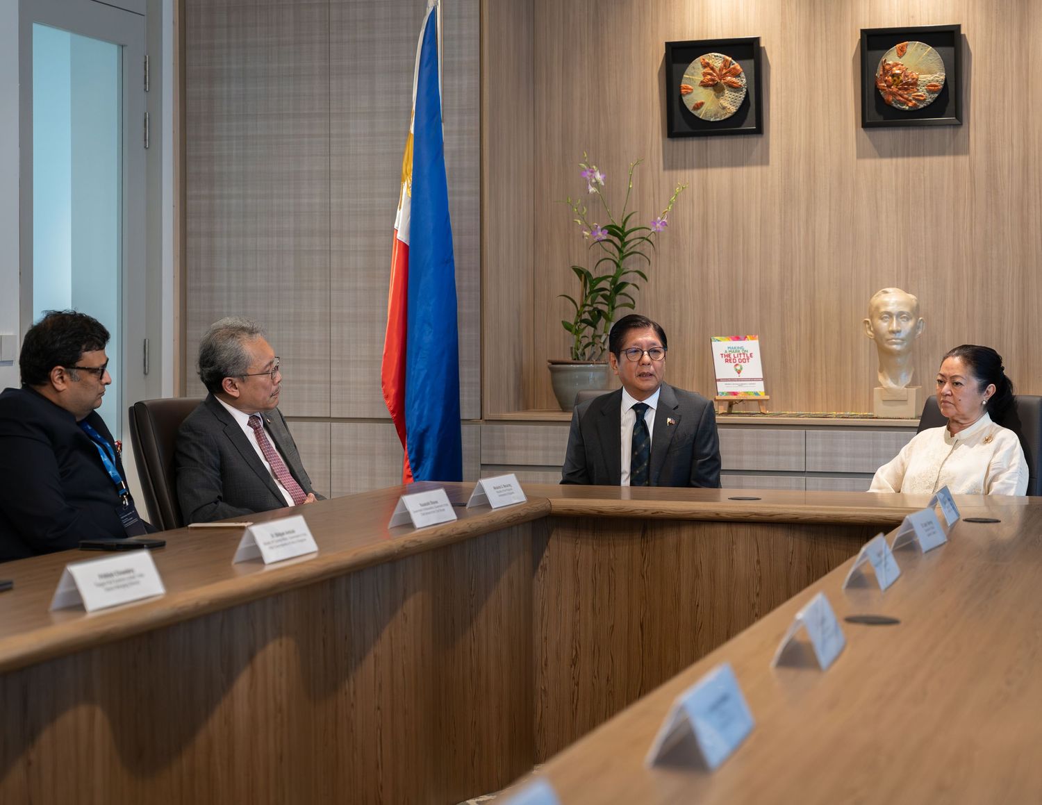 Four professionals seated at conference table with Philippine flag in background.