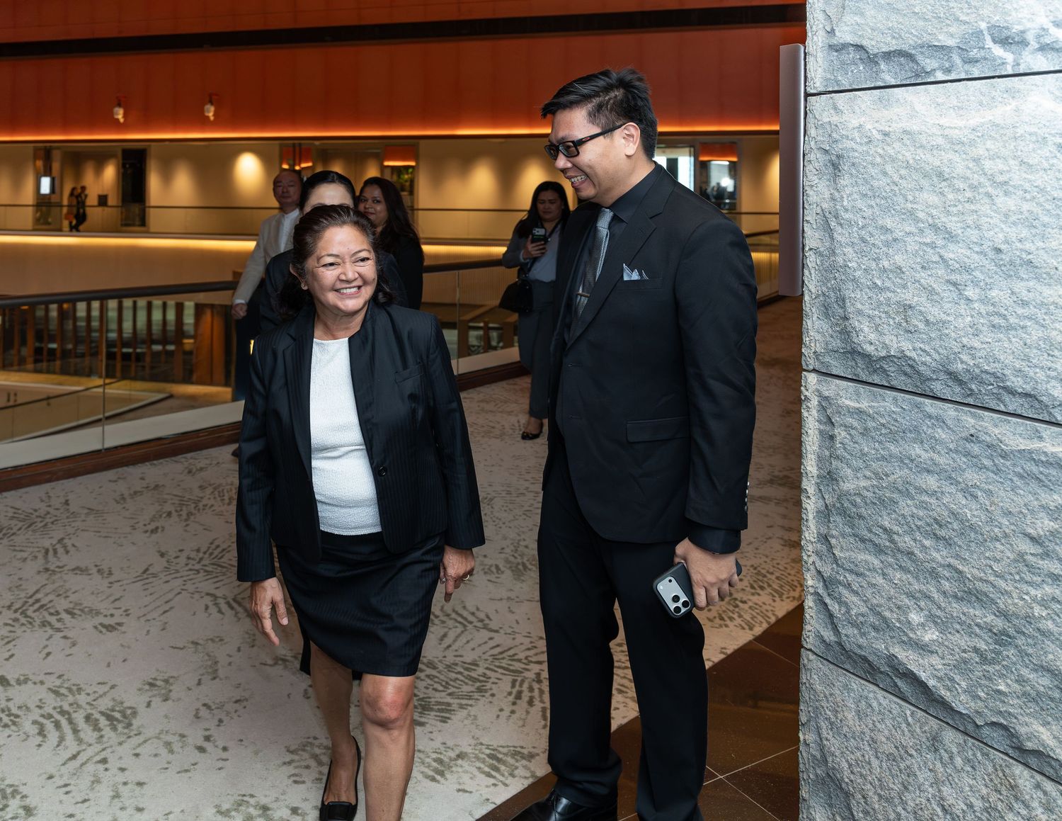 Two professionals in formal business attire walking and conversing in a modern building lobby.
