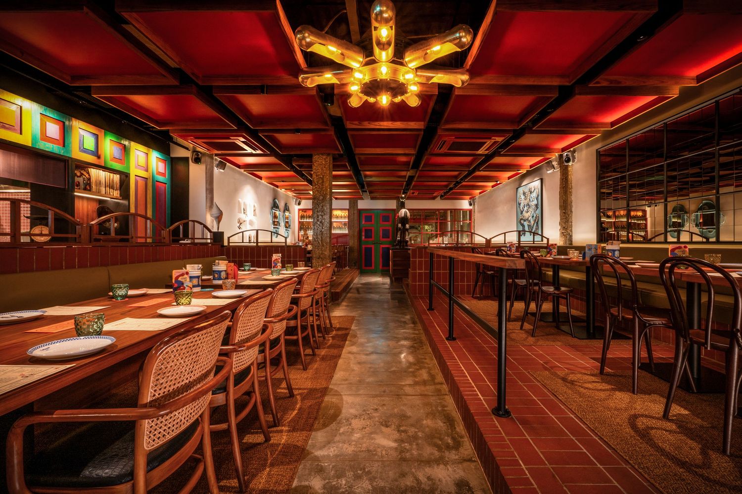 Elegant restaurant interior with warm red lighting, wooden chairs, long dining tables, and ornate chandelier.