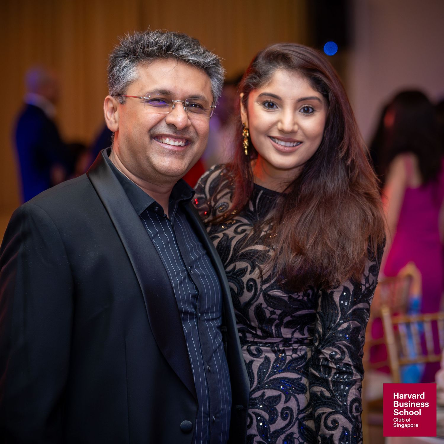 Two elegantly dressed individuals smiling at a Harvard Business School Club of Singapore formal event.