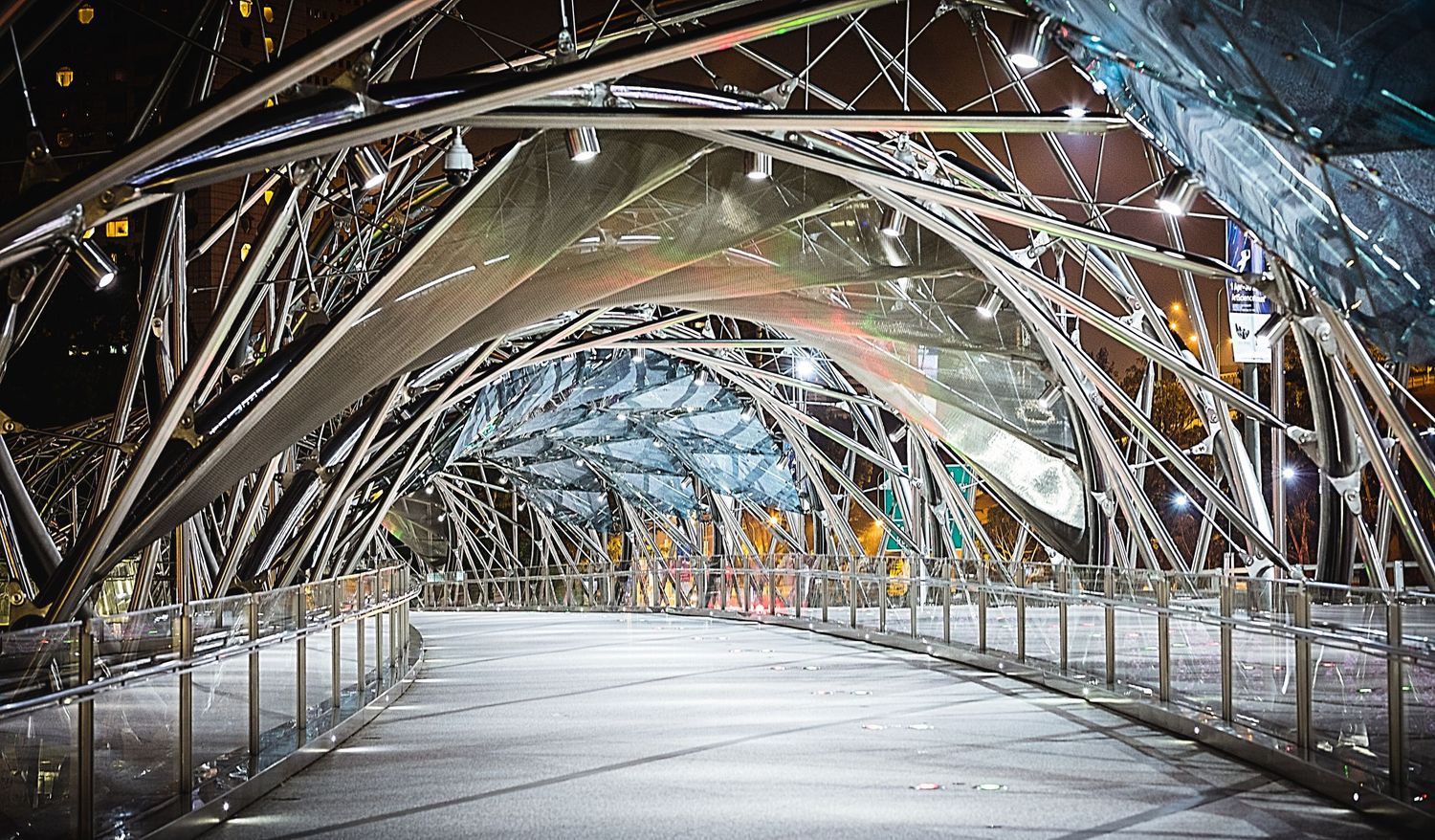 Futuristic steel Helix Bridge in Singapore illuminated at night with curved metallic archways.