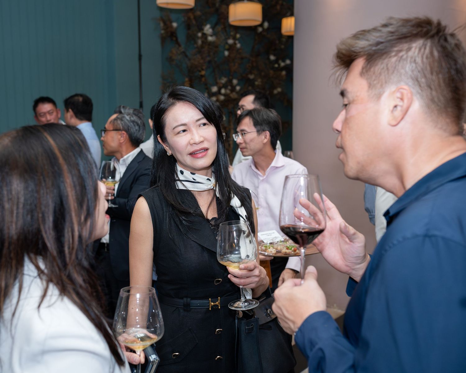 Guests networking at a social event, holding wine glasses and engaging in conversation in an elegant venue.