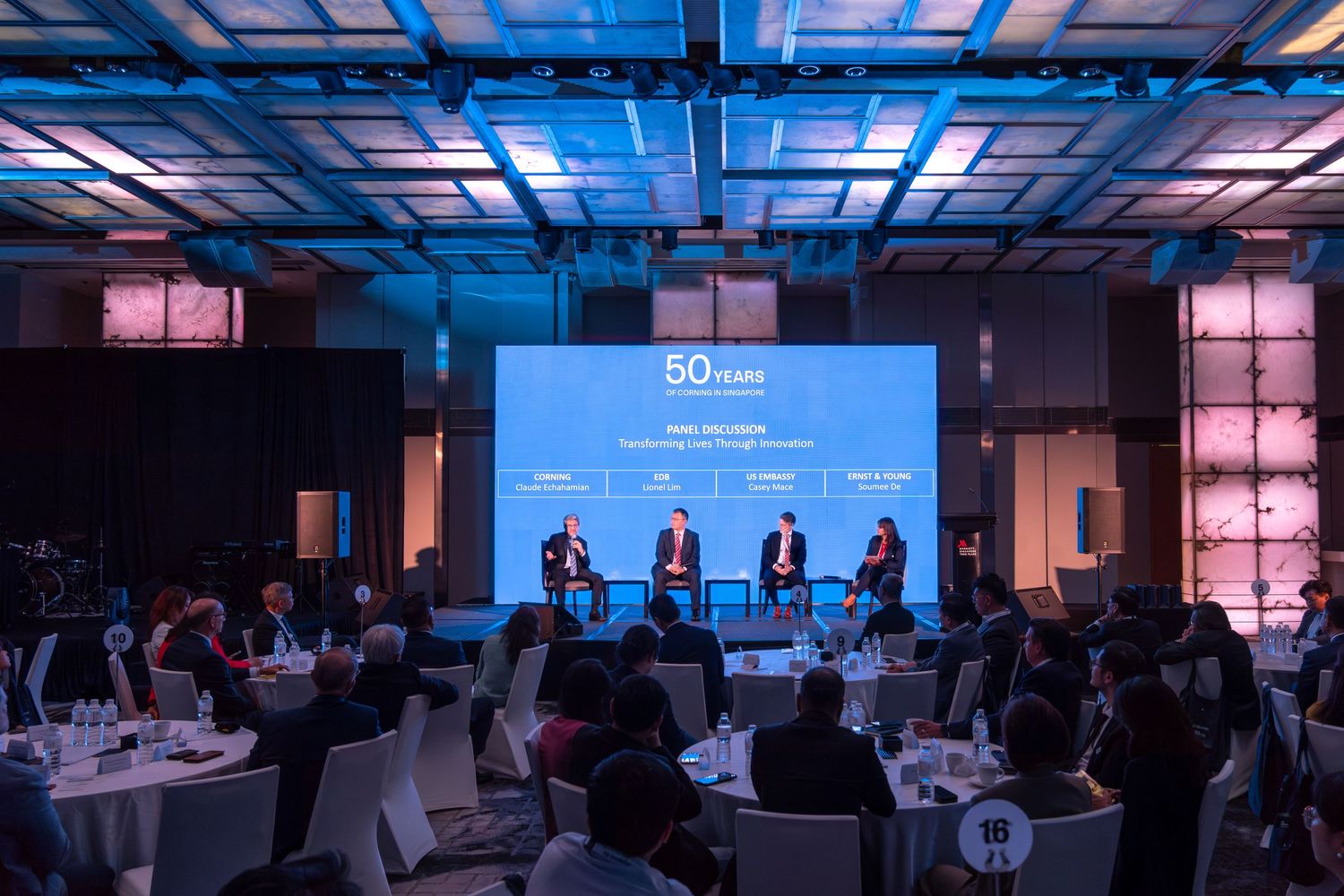 Panel of speakers on stage at a 50th anniversary corporate event in a modern conference ballroom.