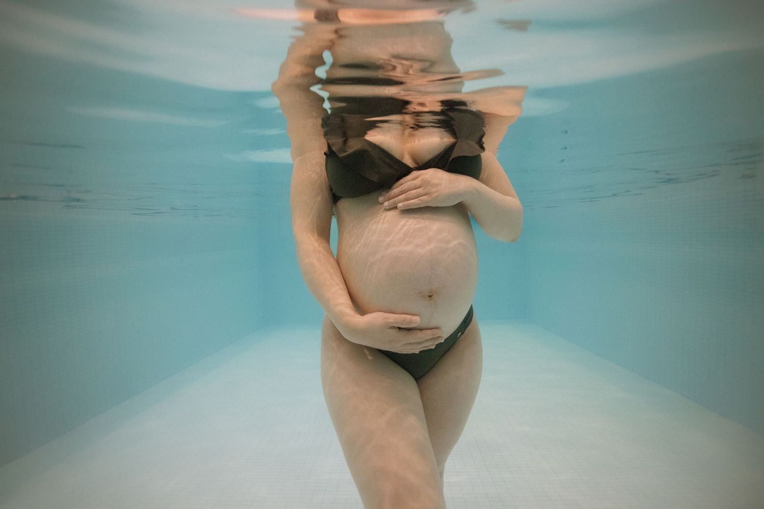 Séance grossesse aquatique à Vevey, future maman dans l’eau avec les mains sur le ventre