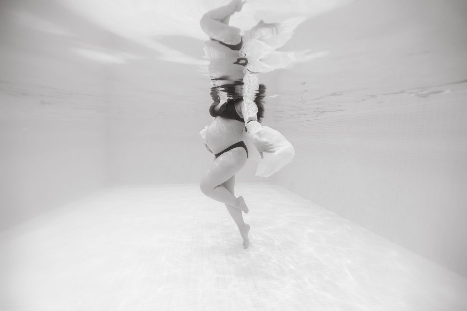 Séance photo aquatique à Vevey, future maman nageant sous l’eau dans un bassin intérieur