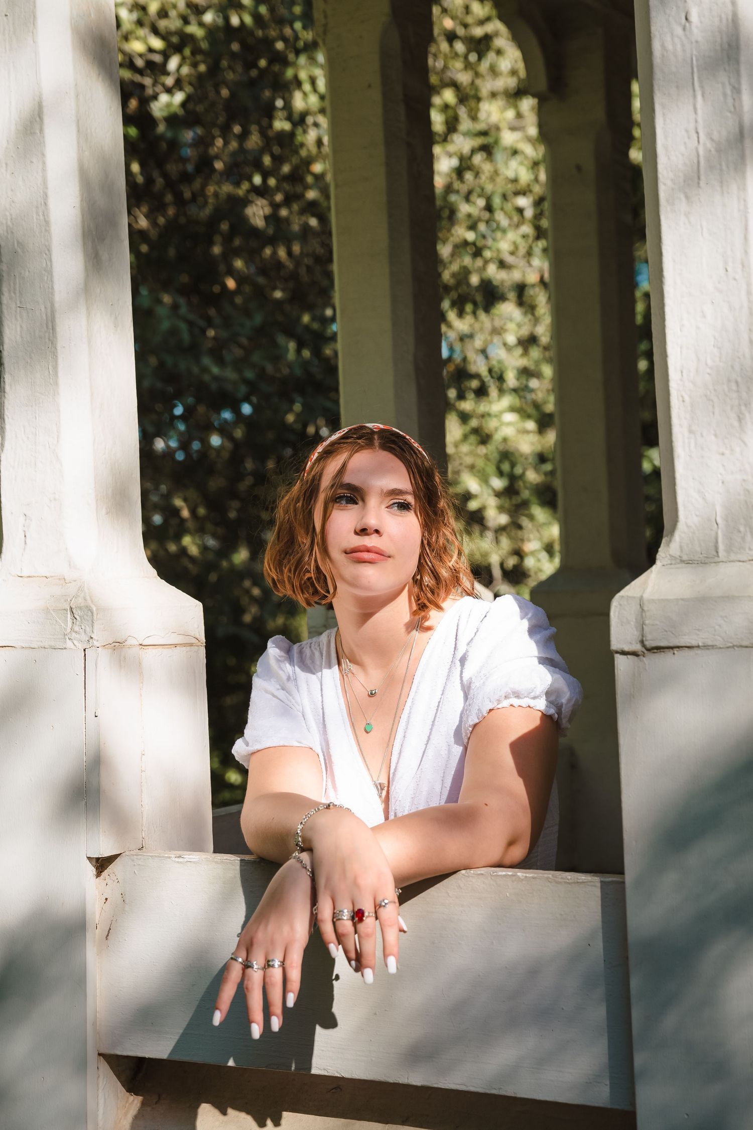 A person in white dress poses between classical columns in natural lighting.