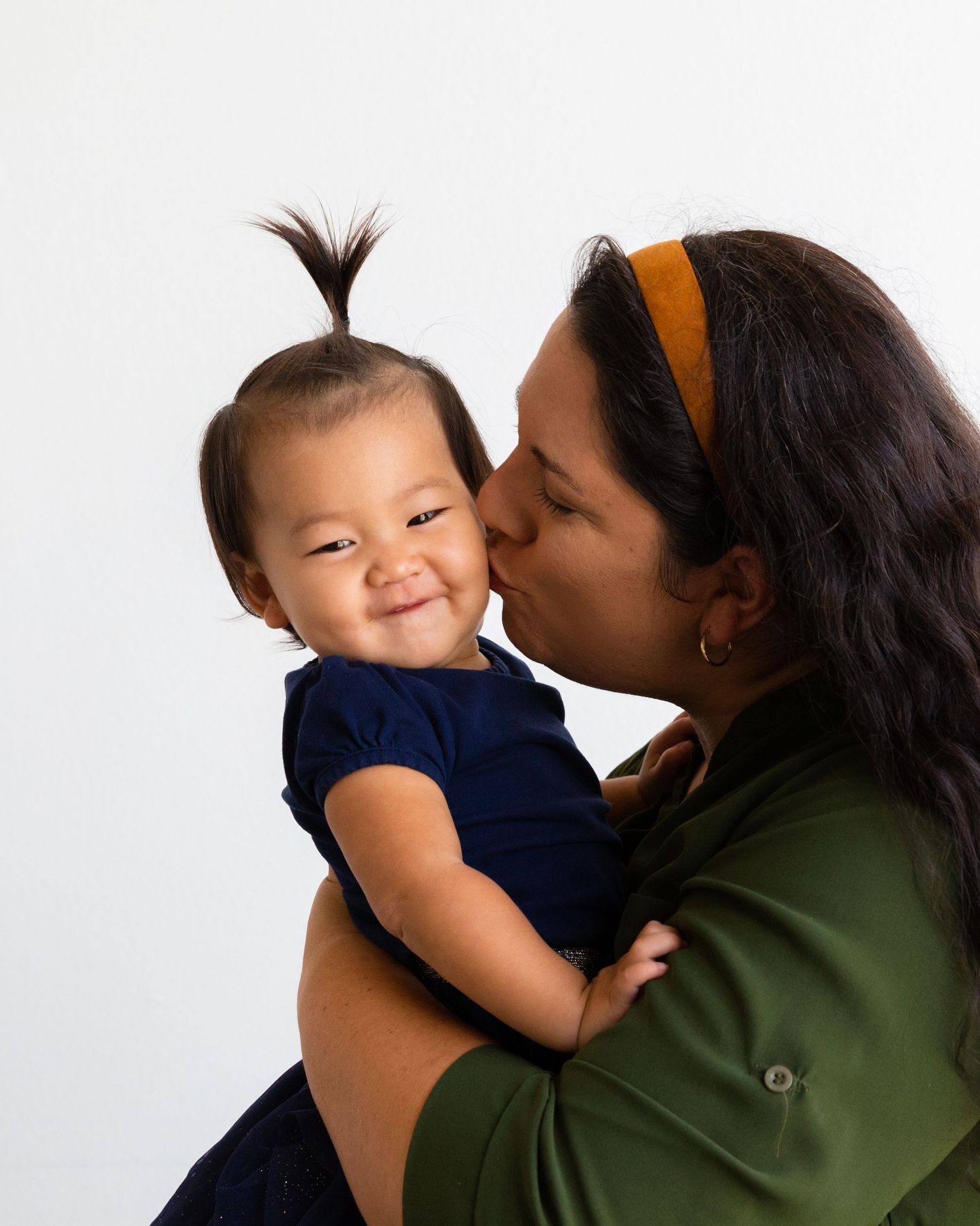 Tender moment between parent and smiling baby in navy blue outfit against white background.