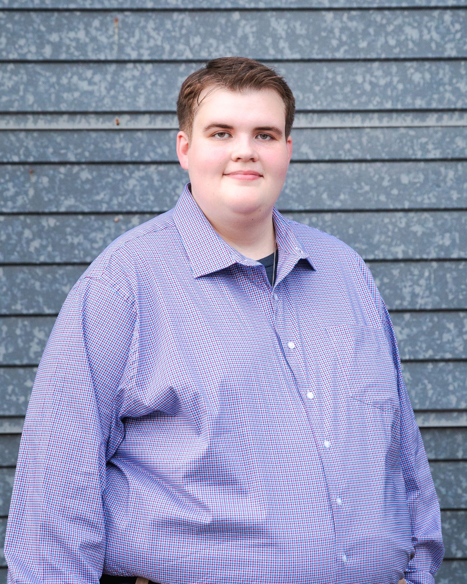 Portrait series of person in purple checkered dress shirt against gray wall background.