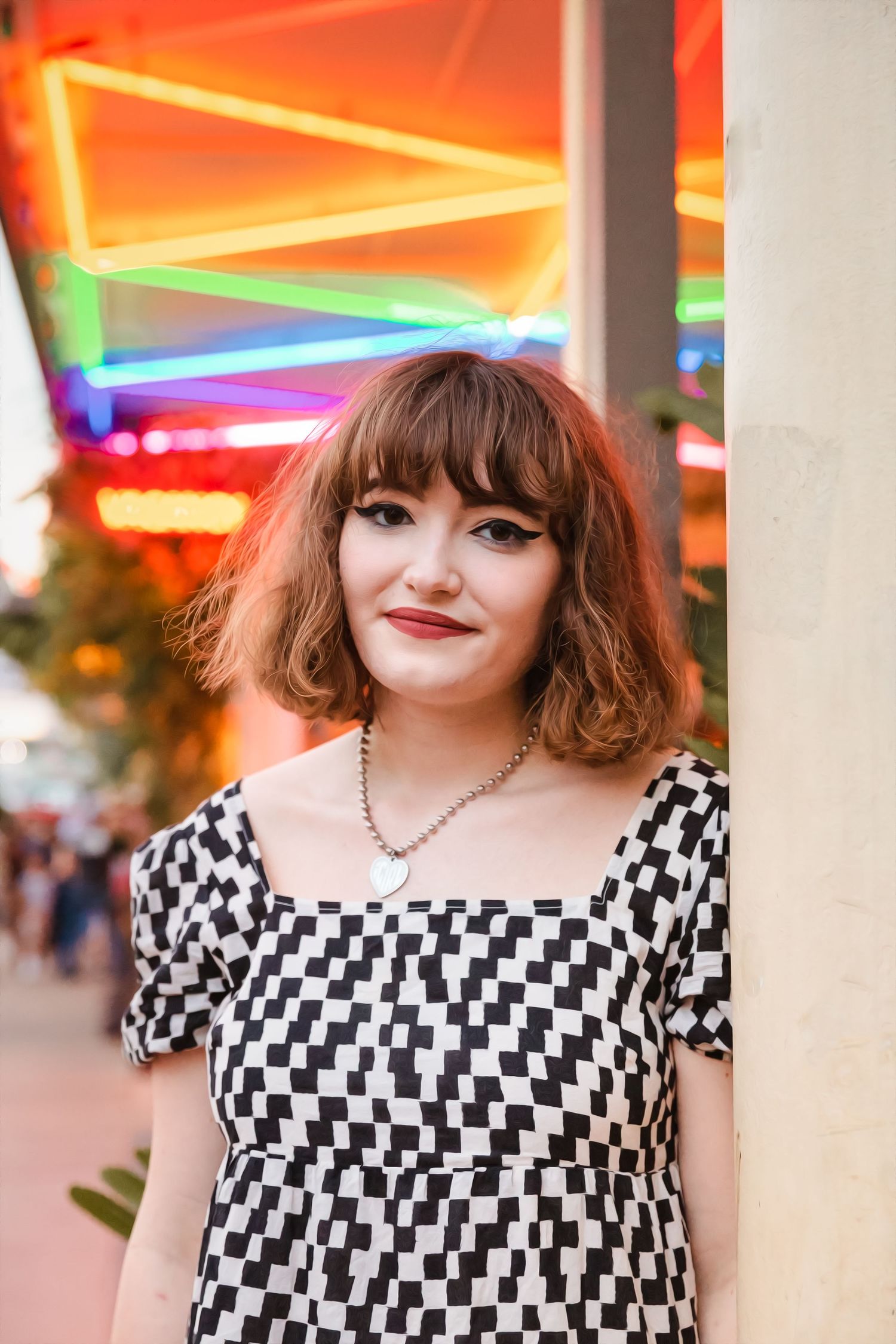 Senior portrait session in Austin, TX. Person wearing a black and white checkered dress posing under colorful neon lights.