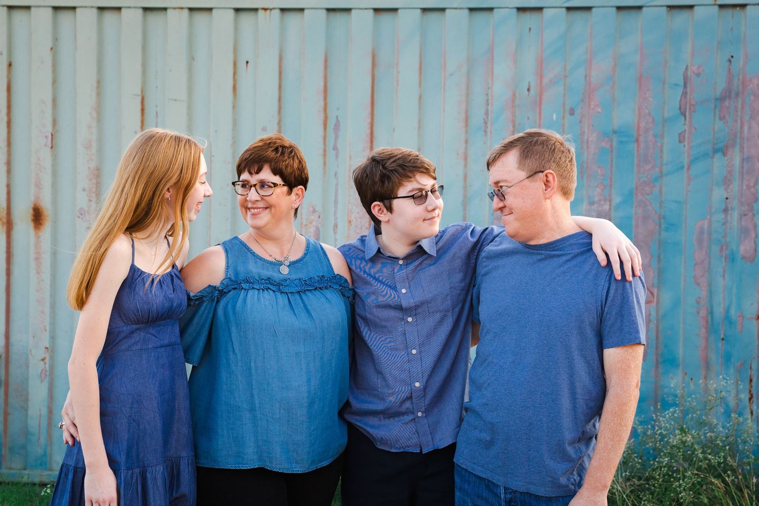 Group wearing coordinated blue outfits posing against a wooden fence backdrop.