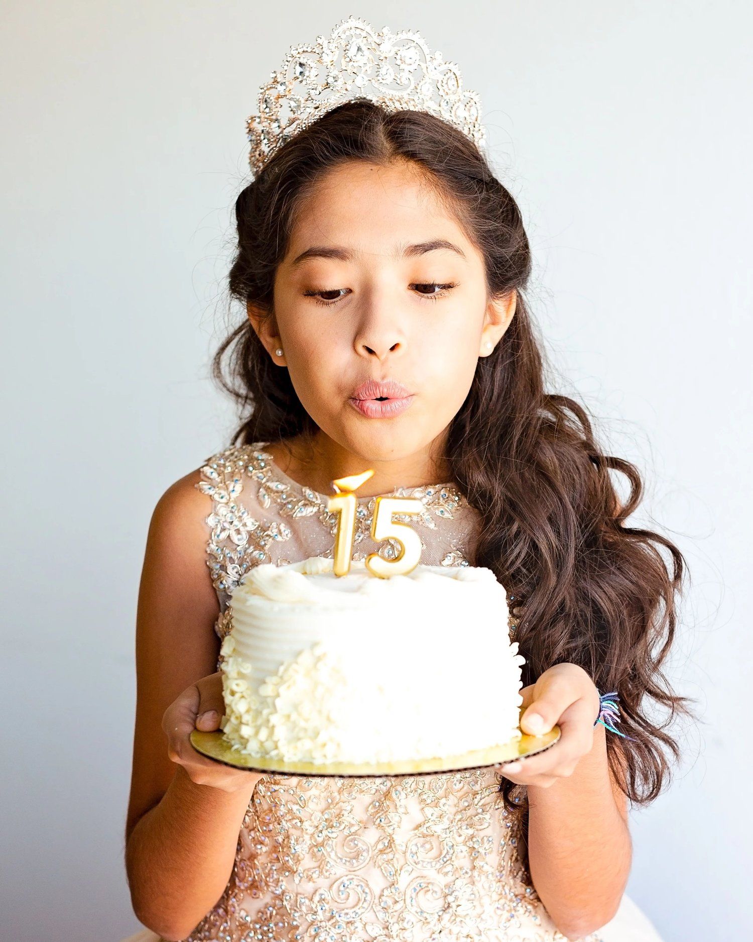 Young person in sparkly dress blowing out candles on white birthday cake.
