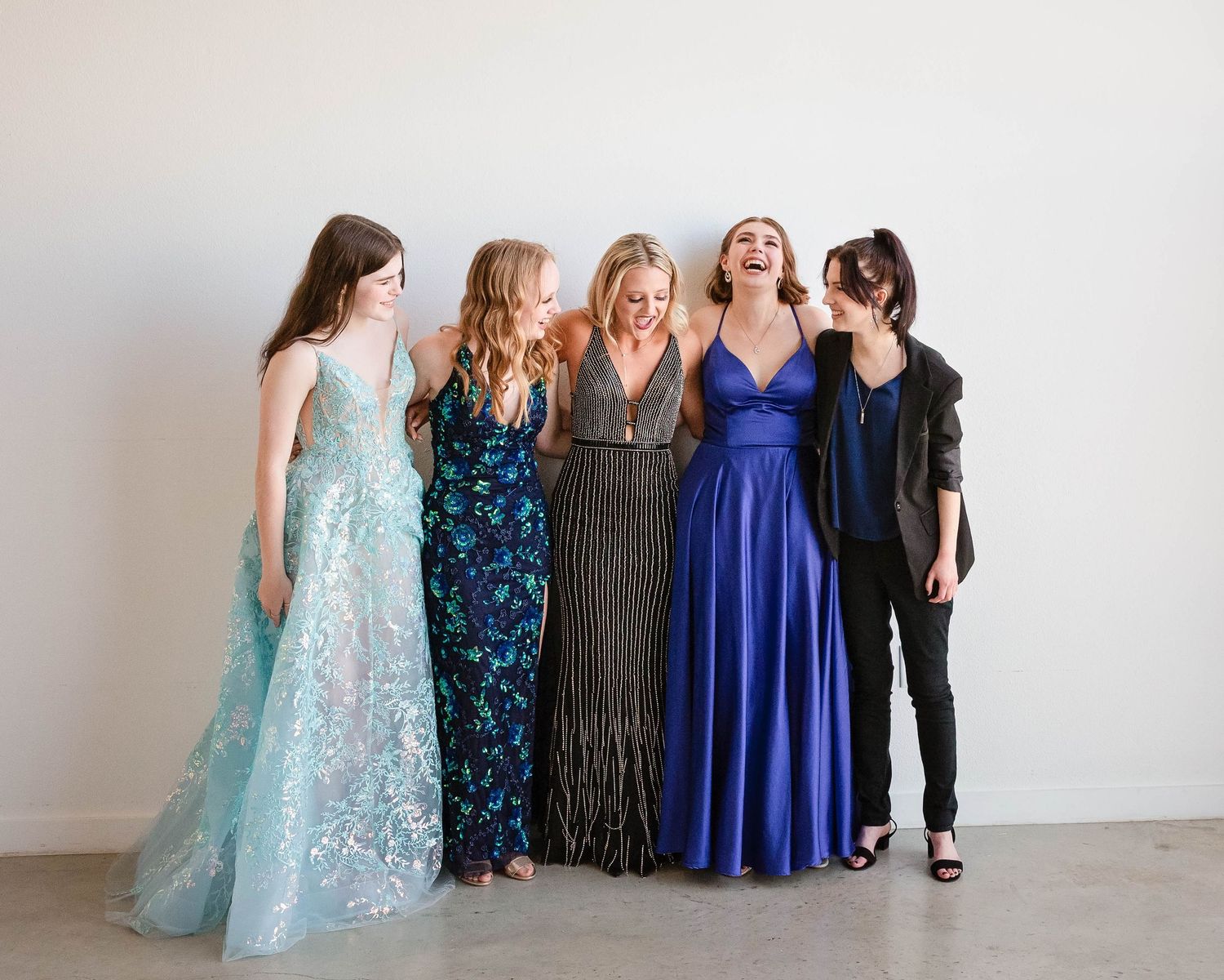 Group portrait against white backdrop with beautiful young women wearing coordinated formal prom dresses in blue tones. Senior high school