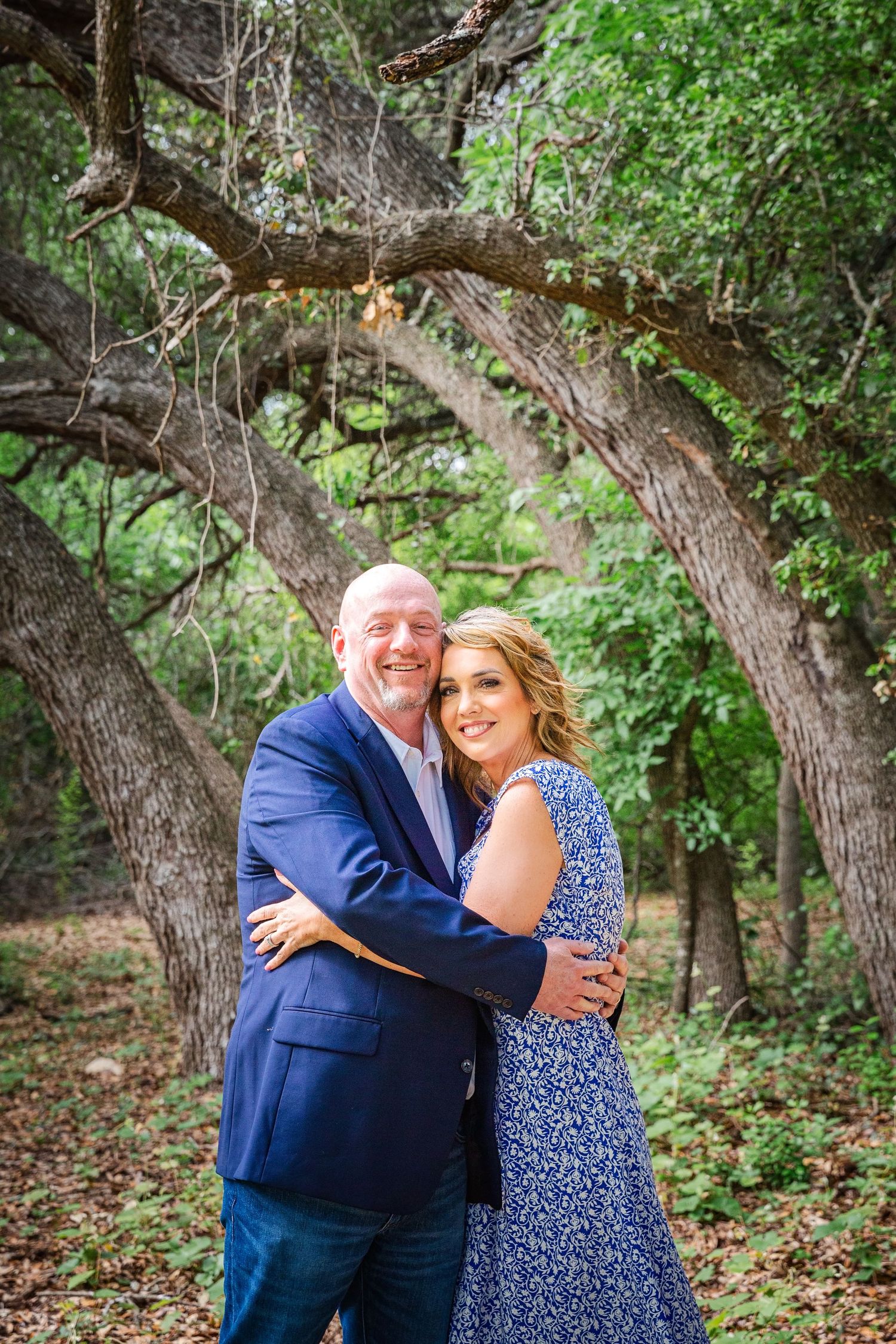 Couple shares intimate moment among trees in wooded outdoor setting.