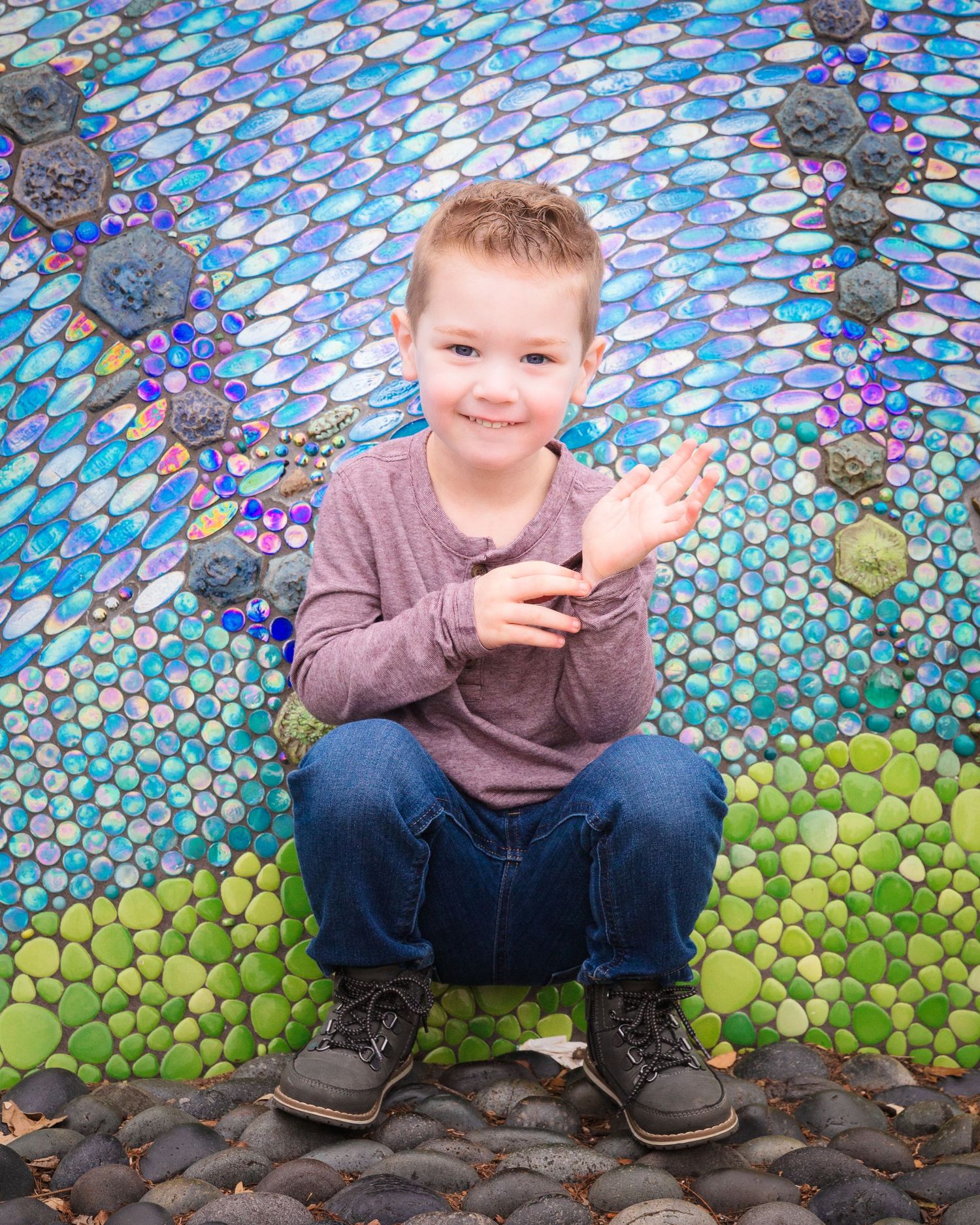 Young child sitting on colorful mosaic tile ground making playful expressions.