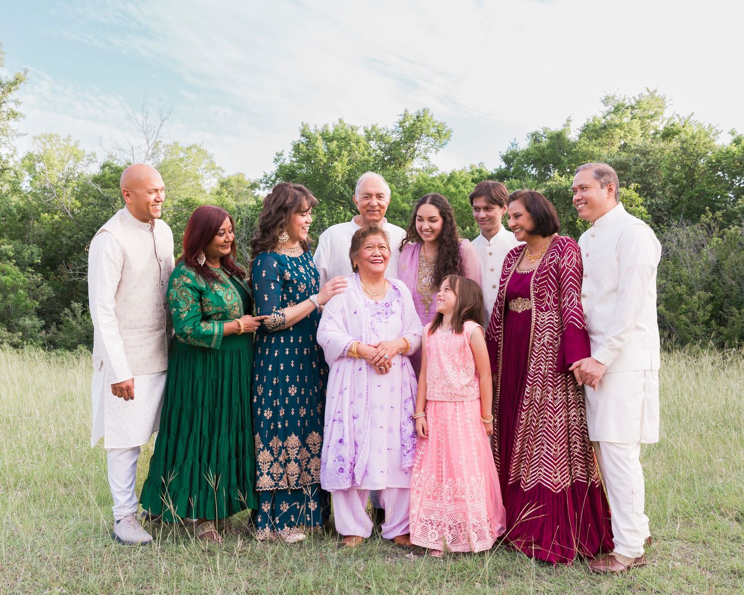 Extended family group photo in coordinated outfits of green, white and pink in an outdoor field setting.