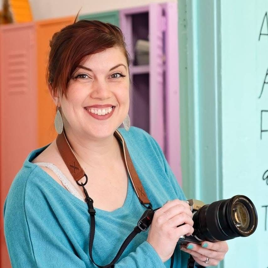 Portrait in teal sweater holding professional camera equipment.