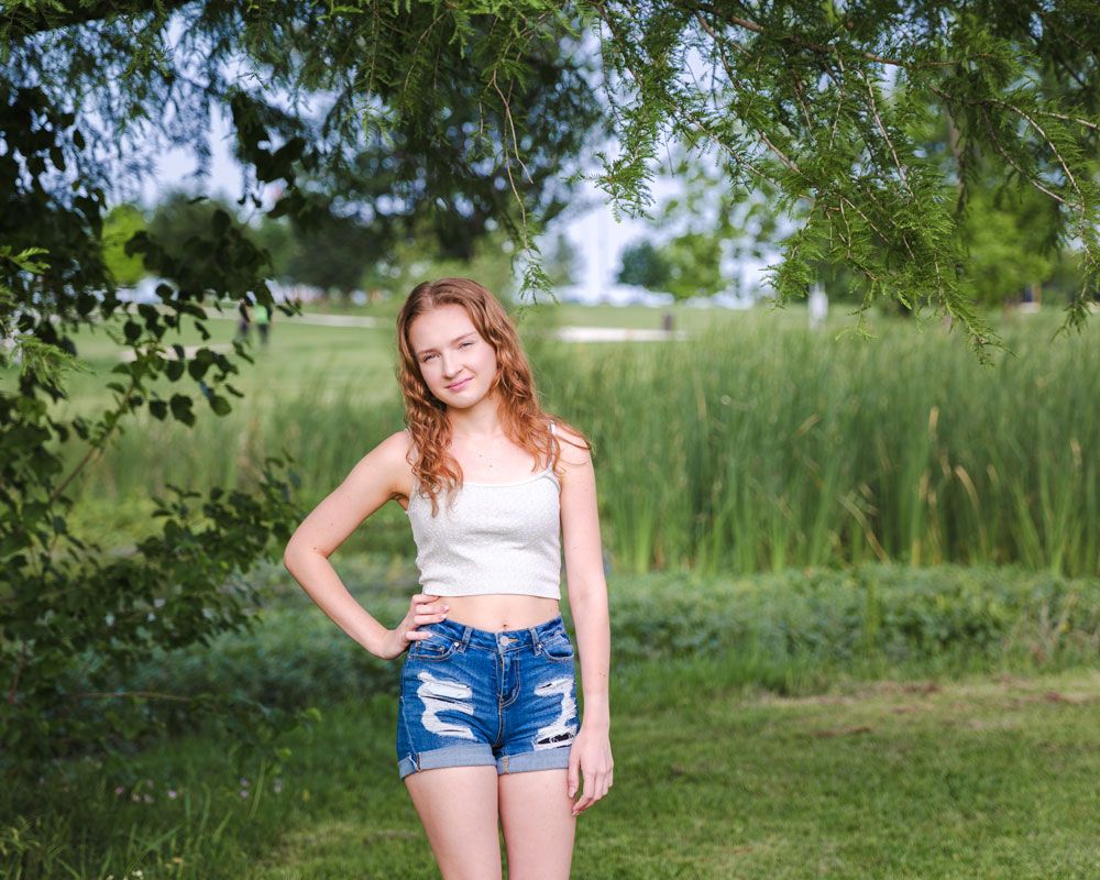 A person in denim shorts poses in front of a lush green outdoor background.