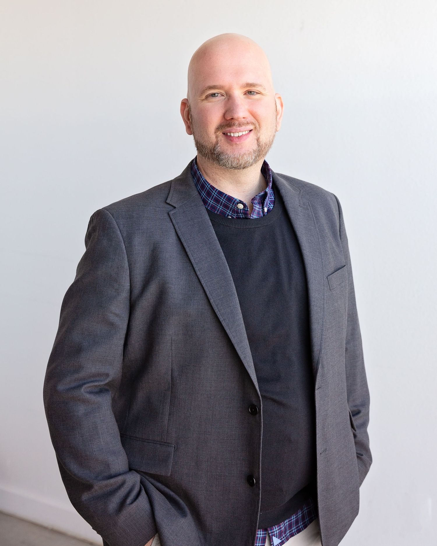Professional headshot of someone wearing a gray suit jacket and black sweater against light background.