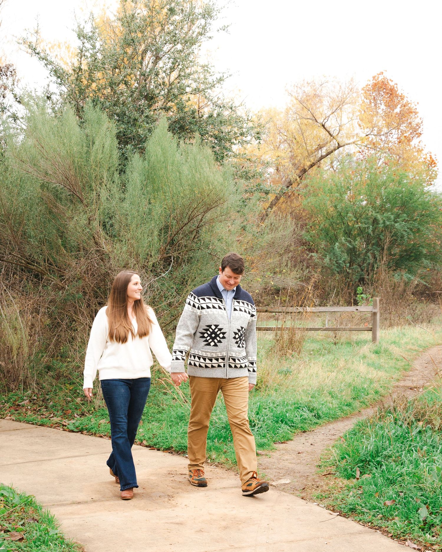 A couple walks hand in hand down a nature trail carrying a patterned blanket.