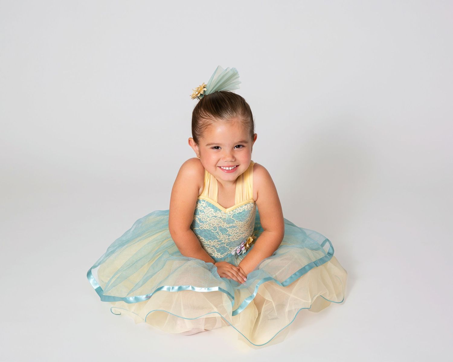 Young dancer in a mint green and cream tulle dress sits gracefully on the floor.