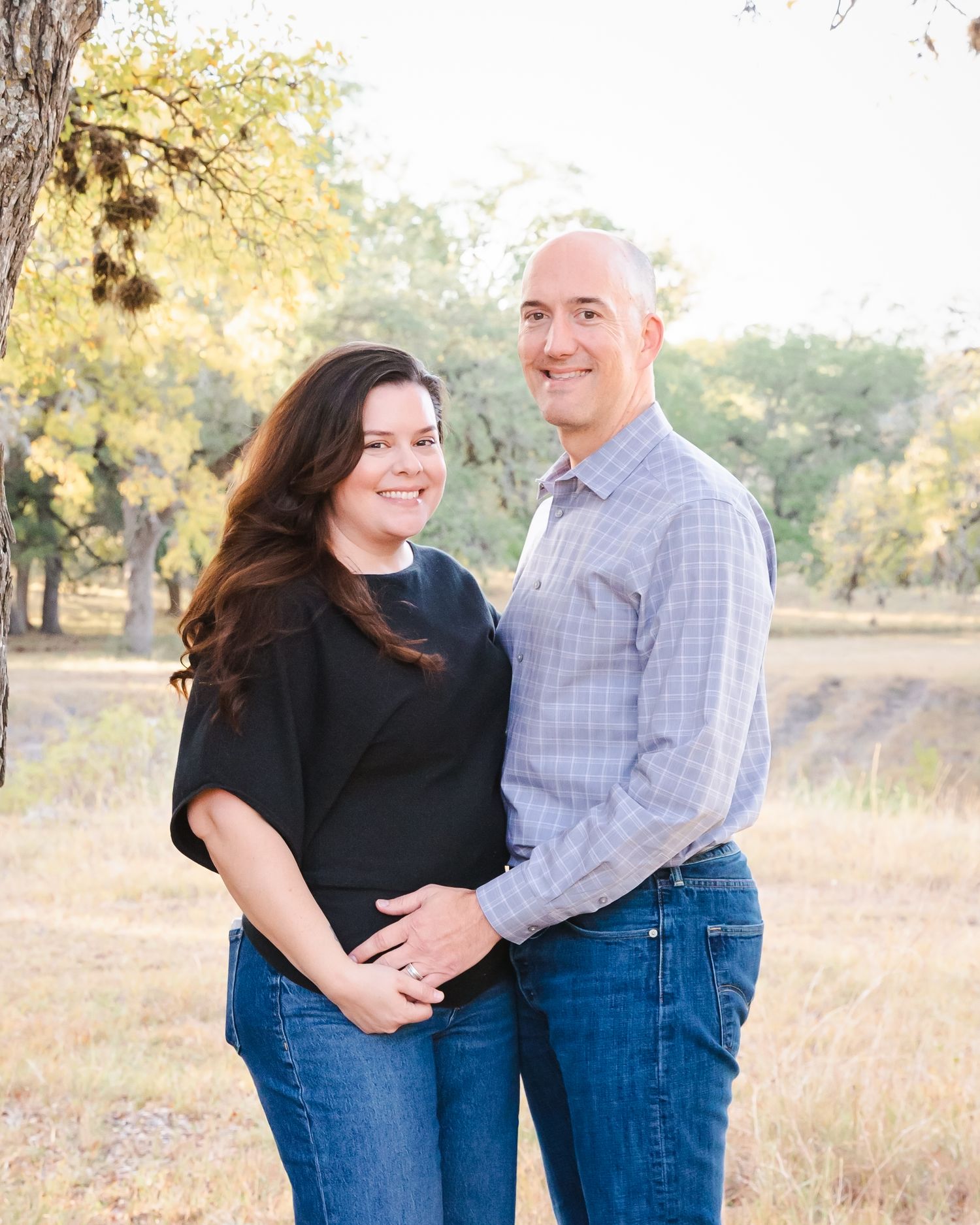 Romantic couple embraces in a sun-lit field during golden hour photo session.
