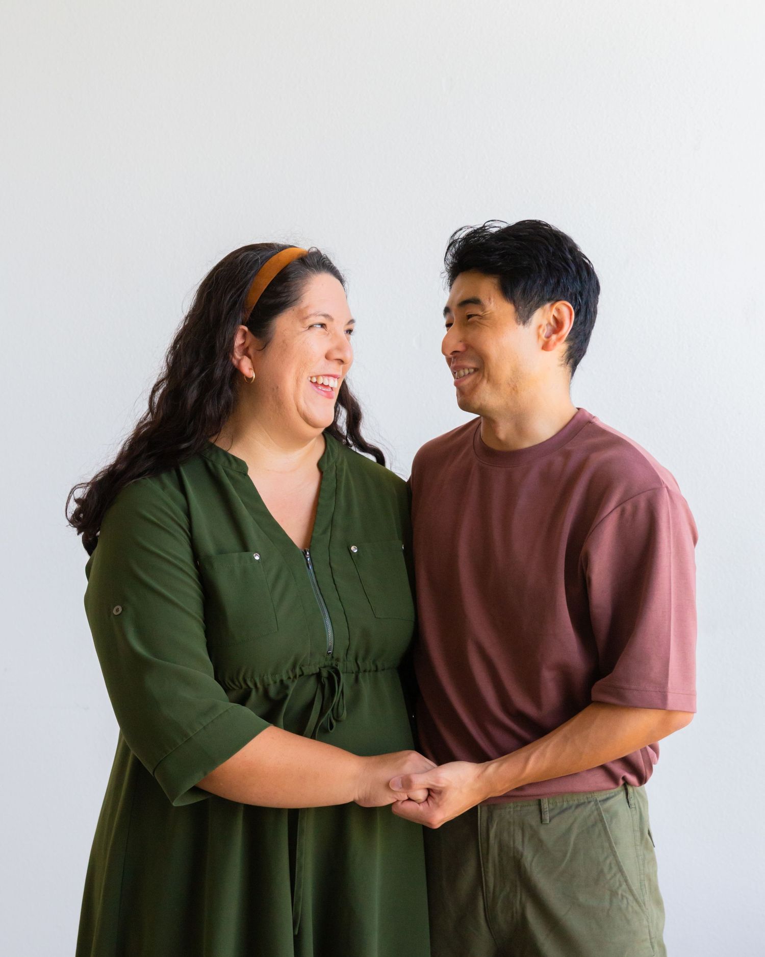 Couple in casual attire sharing joyful moments against white background in studio setting.